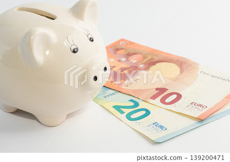 Piggy bank in the shape of a pig with two 20 and 10 euro banknotes next to each other on a white background Piggy bank in the shape of a pig with two 20 and 10 euro banknotes next to each other on a white background 139200471