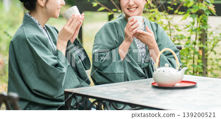 一位年輕的亞洲女子身穿浴衣,在旅途中一邊喝茶一邊享受森林浴。 一位年輕的亞洲女子身穿浴衣,在旅途中一邊喝茶一邊享受森林浴。 139200521