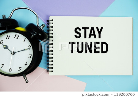 Stay Tuned text written on notepad with alarm clock flat lay on multicolor pastel background 139200700