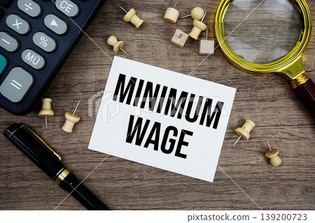 Minimum Wage text written on notepad with pen, magnifying glass and calculator on wooden background 139200723