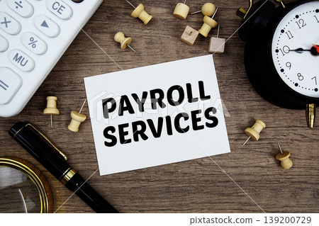 Payroll Services text written on notepad with pen, alarm clock, magnifying glass and calculator on wooden background Payroll Services text written on notepad with pen, alarm clock, magnifying glass and calculator on wooden background 139200729