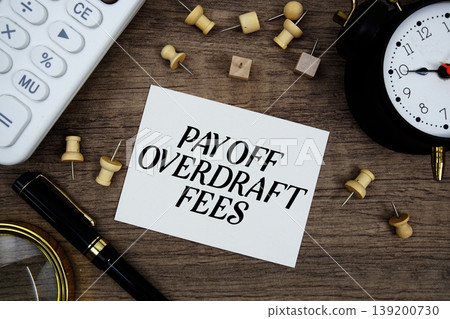 Pay Off Overdraft Fees text written on notepad with pen, alarm clock, magnifying glass and calculator on wooden background Pay Off Overdraft Fees text written on notepad with pen, alarm clock, magnifying glass and calculator on wooden background 139200730