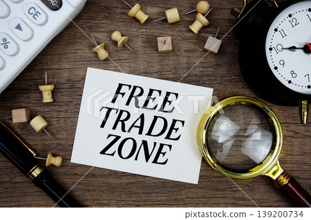 Free Trade Zone text written on notepad with pen, alarm clock, magnifying glass and calculator on wooden background Free Trade Zone text written on notepad with pen, alarm clock, magnifying glass and calculator on wooden background 139200734