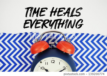 Time Heals Everything text written on paper rip with alarm clock flat lay on blue chevron background Time Heals Everything text written on paper rip with alarm clock flat lay on blue chevron background 139200774