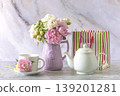 Happy birthday or mothers day still life; bouquet of pink and white peony flowers, white cup of tea, tea pot, gift bag on a marble background; 139201281