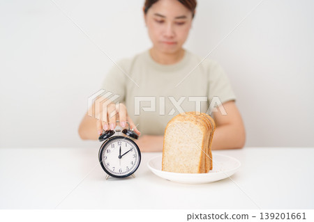 hungry woman with whole wheat bread and clock. concept of intermittent fasting, IF, meal, Time to eat, choosing healthy carbohydrates, balanced diet and weight loss management, Nutrition schedule hungry woman with whole wheat bread and clock. concept of intermittent fasting, IF, meal, Time to eat, choosing healthy carbohydrates, balanced diet and weight loss management, Nutrition schedule 139201661