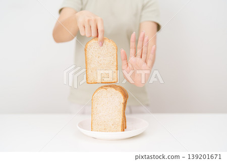 Unhappy woman showing Rejecting gesture and refusing to eat bread. concept of gluten intolerance, gluten sensitivity, carb loading concerns, or a disliking for unhealthy dietary habits Unhappy woman showing Rejecting gesture and refusing to eat bread. concept of gluten intolerance, gluten sensitivity, carb loading concerns, or a disliking for unhealthy dietary habits 139201671