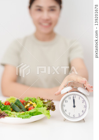 happy smiling woman with fresh organic vegetables plate and alarm clock. intermittent fasting, IF, meal time, nutrition, weight loss, clean eating, Healthy food eating, Wellness, dieting and lifestyle 139201678