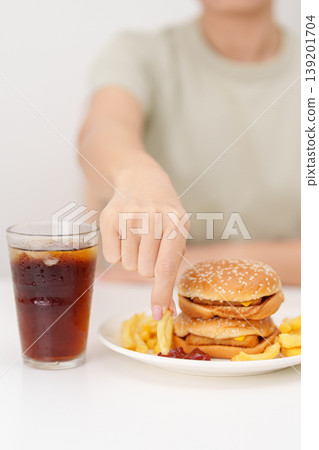 woman eating Juicy beef burger with melted cheddar cheese, potato chips and carbonated Soft drinks. Unhealthy, High calorie, Fast food craving, Obesity, diet, weight loss, junk food and lifestyle 139201704