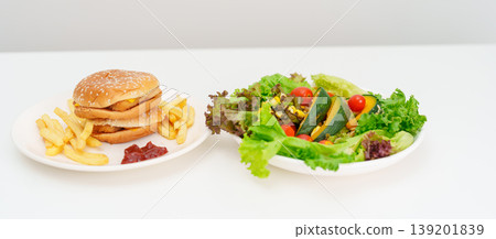 Healthy and Unhealthy Food Choice. Comparison of Calories and Nutrition of vegetables Salad plate and Hamburger. Concept for diet planning, weight loss management, junk food and habit lifestyle Healthy and Unhealthy Food Choice. Comparison of Calories and Nutrition of vegetables Salad plate and Hamburger. Concept for diet planning, weight loss management, junk food and habit lifestyle 139201839