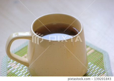 Close up of a warm ceramic mug filled with tea on a green bamboo coaster on a light wooden surface Close up of a warm ceramic mug filled with tea on a green bamboo coaster on a light wooden surface 139201843