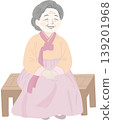 An elderly woman wearing traditional Korean hanbok, seated calmly on a wooden bench. 139201968