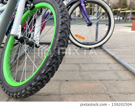 brightly colored children's bicycles parked carelessly in a bicycle parking area at a playground 139202504