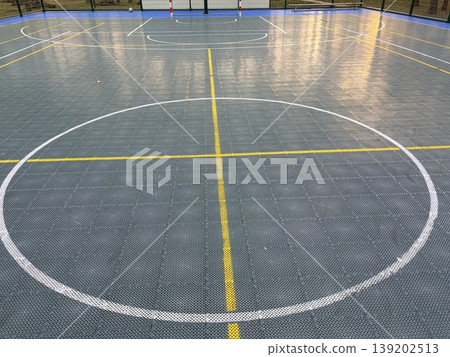 A modern small sports ground for basketball and football is surrounded by a high fence and is located in an open area A modern small sports ground for basketball and football is surrounded by a high fence and is located in an open area 139202513