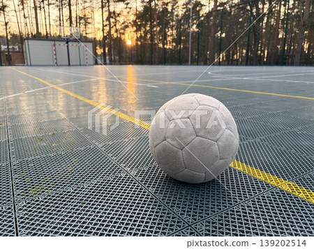 An old soccer ball lies on the artificial surface of a sports stadium in an open wooded area 139202514