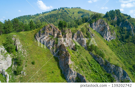 Rocky outcrops dominate verdant Altai Mountains with scattered pine trees under a clear blue summer sky Rocky outcrops dominate verdant Altai Mountains with scattered pine trees under a clear blue summer sky 139202742