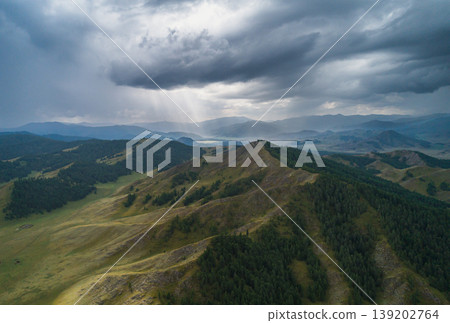 Altai Mountains landscape view with dark storm clouds and sun rays breaking through, illuminating green forest and valleys Altai Mountains landscape view with dark storm clouds and sun rays breaking through, illuminating green forest and valleys 139202764