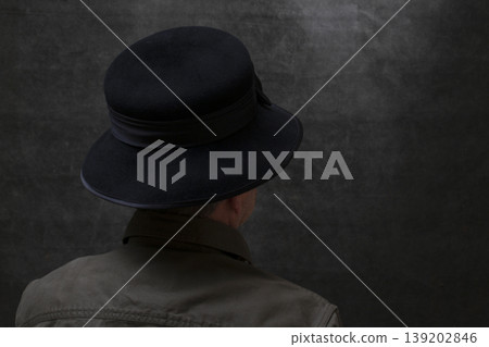A man in a hat stands with his back against a dark background A man in a hat stands with his back against a dark background 139202846