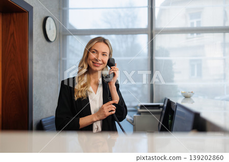 Smiling Female Receptionist Answering Office Phone at Modern Corporate Front Desk Reception Area Smiling Female Receptionist Answering Office Phone at Modern Corporate Front Desk Reception Area 139202860