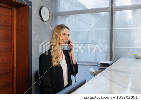 Professional Blonde Receptionist Talking on Telephone Behind Luxury Marble Reception Counter Professional Blonde Receptionist Talking on Telephone Behind Luxury Marble Reception Counter 139202861