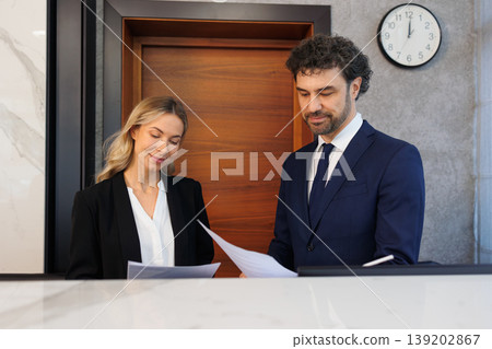 Business Woman and Male Executive Talking While Holding Papers in Office Lobby Business Woman and Male Executive Talking While Holding Papers in Office Lobby 139202867