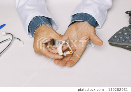 Close up of an Audiologist's hands showing a hearing aid in the hospital clinic. Audiology concept. 139202981