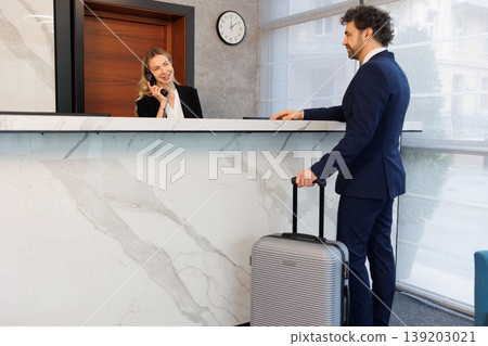 Elegant Hotel Receptionist Assisting Business Traveler During Check In at Modern Lobby Desk Elegant Hotel Receptionist Assisting Business Traveler During Check In at Modern Lobby Desk 139203021