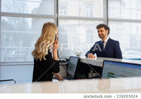 Friendly Receptionist on Phone Assisting Guest at Stylish Hotel Front Desk Interior Friendly Receptionist on Phone Assisting Guest at Stylish Hotel Front Desk Interior 139203024