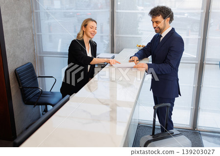 Friendly Hotel Receptionist Explaining Registration Form to Business Traveler at Counter 139203027