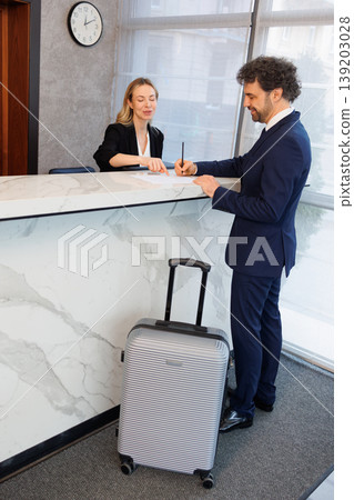Business Guest Signing Check In Papers with Receptionist Guidance at Hotel Front Desk Business Guest Signing Check In Papers with Receptionist Guidance at Hotel Front Desk 139203028