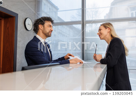 Friendly conversation between hotel receptionist and female guest at reception desk Friendly conversation between hotel receptionist and female guest at reception desk 139203045