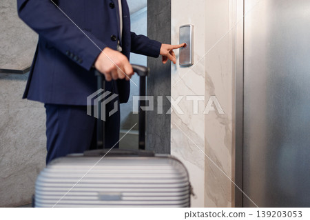 Close up of businessman pressing elevator button with suitcase handle Close up of businessman pressing elevator button with suitcase handle 139203053
