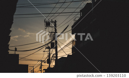 黃昏時分,電線桿和電線的輪廓在居民區若隱若現。 黃昏時分,電線桿和電線的輪廓在居民區若隱若現。 139203110