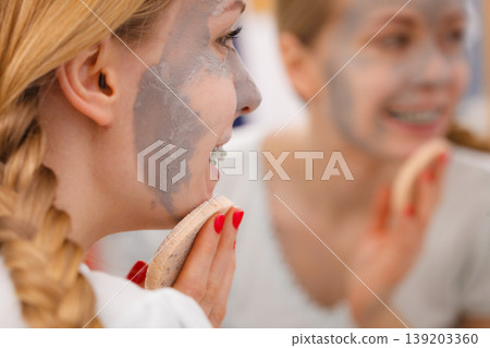 Woman removing mud facial mask with sponge Woman removing mud facial mask with sponge 139203360