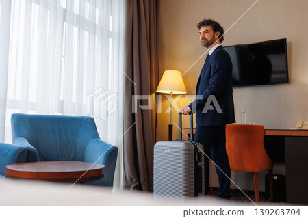 Serious Executive Standing With Luggage In Hotel Room Interior Serious Executive Standing With Luggage In Hotel Room Interior 139203704