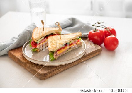 Club sandwich with ham, cheese, tomatoes, lettuce, cucumber on a wooden board on a white table Club sandwich with ham, cheese, tomatoes, lettuce, cucumber on a wooden board on a white table 139203903