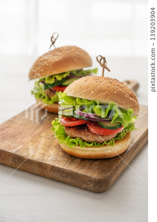 A delicious homemade burger with beef, tomato, cheese, and lettuce on a cutting board on a table A delicious homemade burger with beef, tomato, cheese, and lettuce on a cutting board on a table 139203904