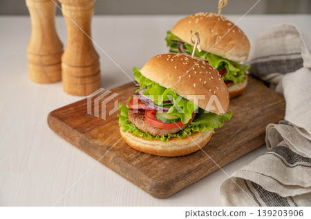 A homemade burger with beef, tomato, cheese, and lettuce on a cutting board on a white table A homemade burger with beef, tomato, cheese, and lettuce on a cutting board on a white table 139203906