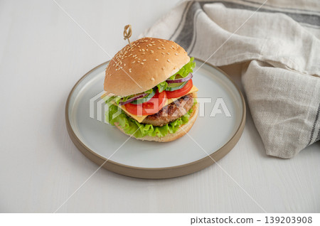 Beef burger with tomato, cheese, and lettuce on a plate on a light wooden background with napkin. Beef burger with tomato, cheese, and lettuce on a plate on a light wooden background with napkin. 139203908