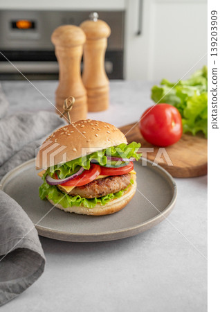 Beef burger with tomato, cheese, and lettuce on a plate on a kitchen table with spice, vegetable Beef burger with tomato, cheese, and lettuce on a plate on a kitchen table with spice, vegetable 139203909