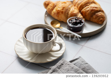 Cup of espresso coffee and fresh croissants on a light background with berry jam and spoon. Cup of espresso coffee and fresh croissants on a light background with berry jam and spoon. 139203912