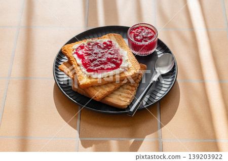 Toast with sweet berry-fruit jam and cream cheese on a dark plate on a yellow tile background Toast with sweet berry-fruit jam and cream cheese on a dark plate on a yellow tile background 139203922