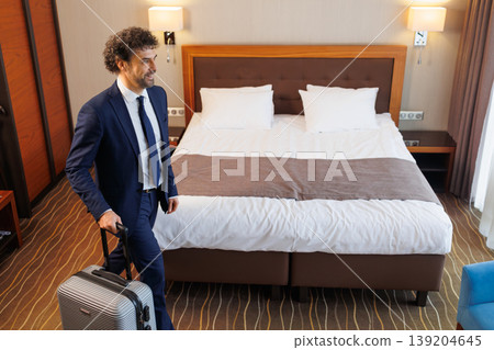 Businessman arriving to hotel room with suitcase and looking at comfortable bed Businessman arriving to hotel room with suitcase and looking at comfortable bed 139204645