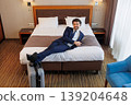 Smiling businessman posing on hotel bed with suitcase after business travel arrival 139204648