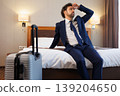 Exhausted Business Traveler Resting on Hotel Bed with Luggage After Long Journey 139204650