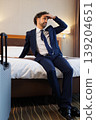 Stressed Businessman Sitting on Bed in Hotel Room Touching Forehead After Workday 139204651