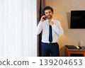 Smiling Businessman Talking on Phone While Adjusting Tie in Hotel Room 139204653