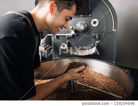 Smiling male worker checking roasted coffee beans at an industrial machine Smiling male worker checking roasted coffee beans at an industrial machine 139204896