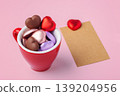 Valentine's Day concept with heart chocolates in red coffee cup and blank brown craft paper card on pink background 139204956