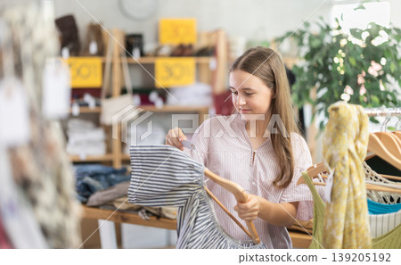 Girl chooses a set of clothes for summer. Visitor to the boutique examines the new summer collection of clothes 139205192